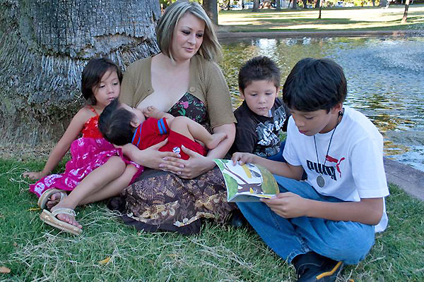 Mother breastfeeding baby at a park with her children